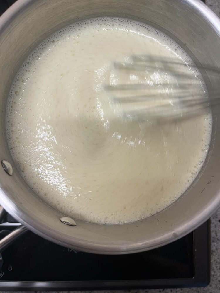 Sobald die Sahne - Milch - Mischung zu kochen beginnt, einen Teil davon auf die Eiermischung gießen und gut mit einem Schneebesen verrühren. Die Mischung wieder zurück in den Topf gießen während ständigem Rühren wieder erhitzten