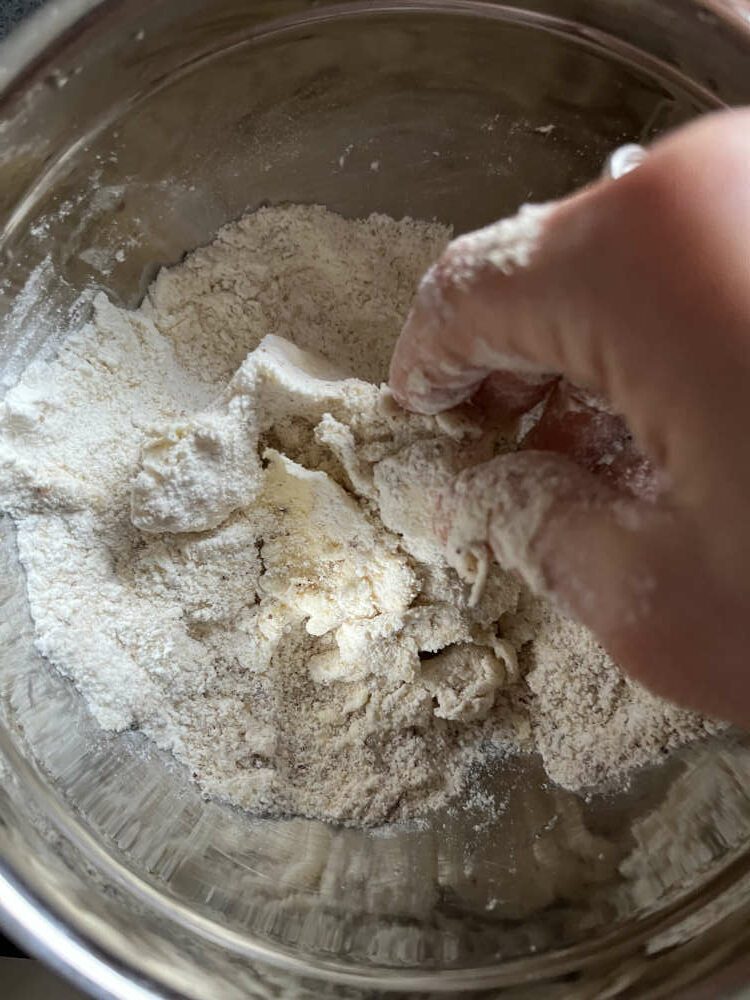 Butter, Zucker, Mandeln und Mehl mit den Händen zu Streuseln verarbeiten