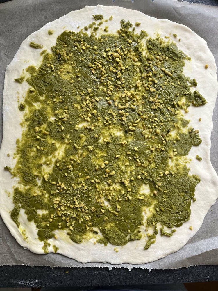 Den Teig mit der Pistazienpaste bestreichen und mit den gehackten Pistazien bestreuen