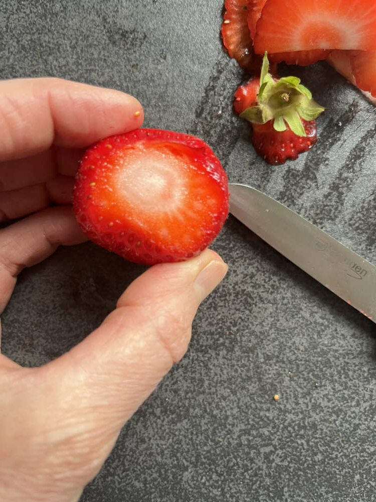 Von den Erdbeeren den Stielansatz gerade abschneiden, dann die Erdbeeren längs halbieren