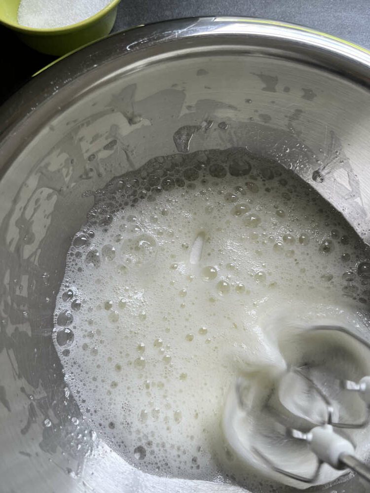 Sobald das Eiweiß große Blasen bildet, ein Drittel des Zuckers unterrühren