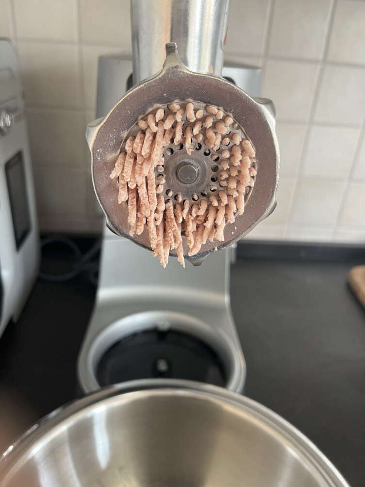 Fleisch, Mortadella und Schinken durch den Fleischwolf geben