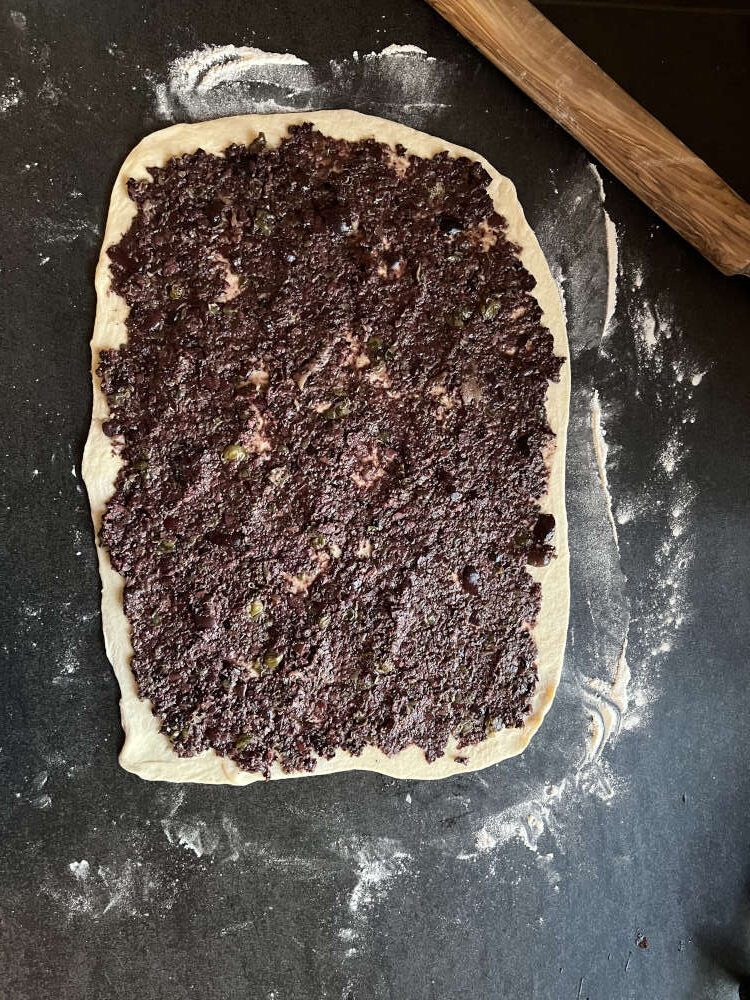 Die Tapenade dünn auf dem Teig verstreichen